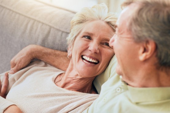 two older people sitting on a sofa, sharing a laugh