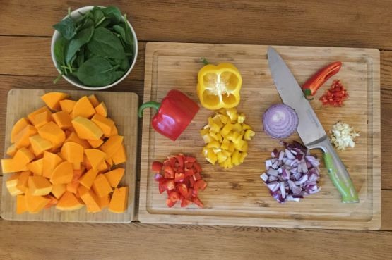 chopped vegetables on a board and a bowl of spinach leaves