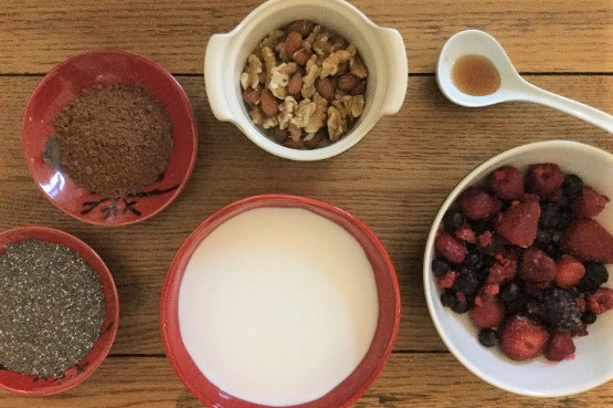 individual bowls of coconut milk, berries, mixed nuts, chocolate, chia seeds and a spoon of honey