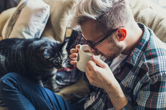 A man sitting on a sofa with his cat, drinking coffee