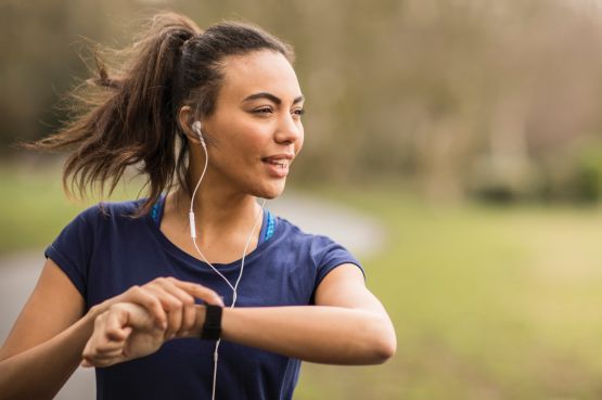 woman running outdoors and looking at her fitbit