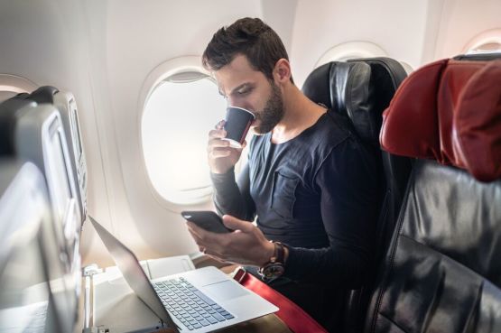 person on an airplane checking phone and laptop