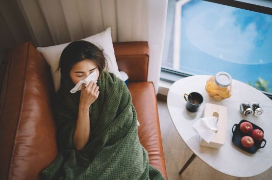 A person blowing their nose, lying on the sofa