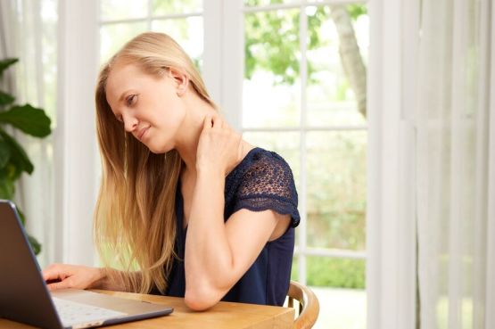 person speaking to a doctor online holding neck in pain