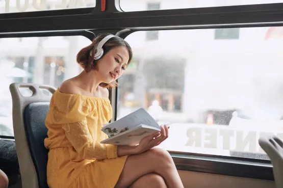 person on a bus reading, with headphones on