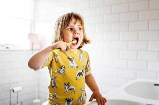 child brushing their teeth in with a yellow toothbrush