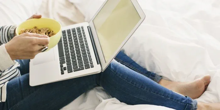 person with a bowl of cereal and laptop on a bed