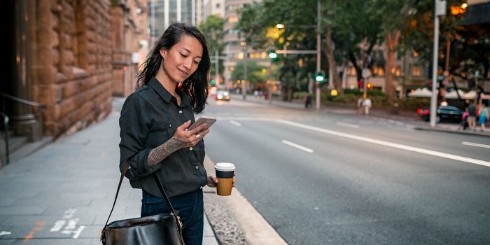 woman checking her phone waiting on a footpath