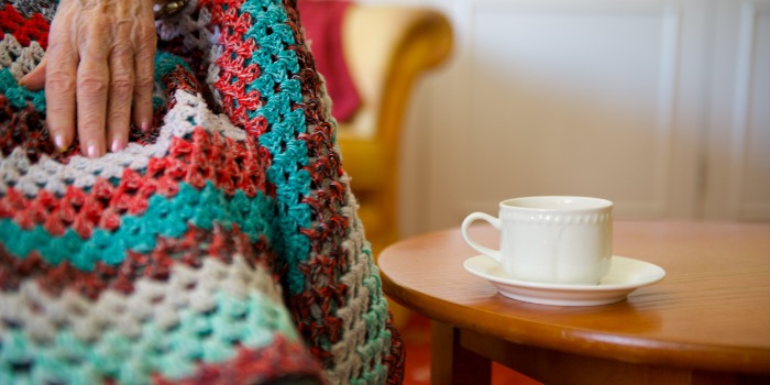 A person sitting with a hot drink, covered in a blanket
