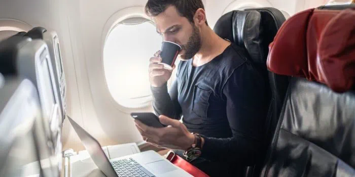 person on an airplane checking phone and laptop