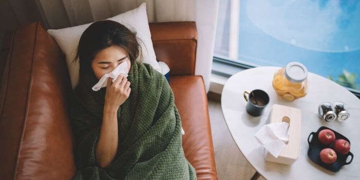 A person blowing their nose, lying on the sofa