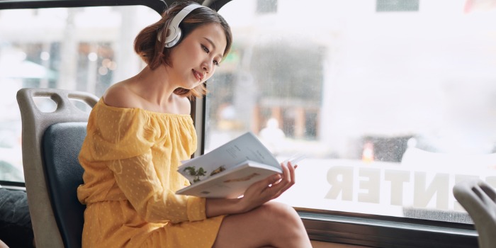 person on a bus reading, with headphones on