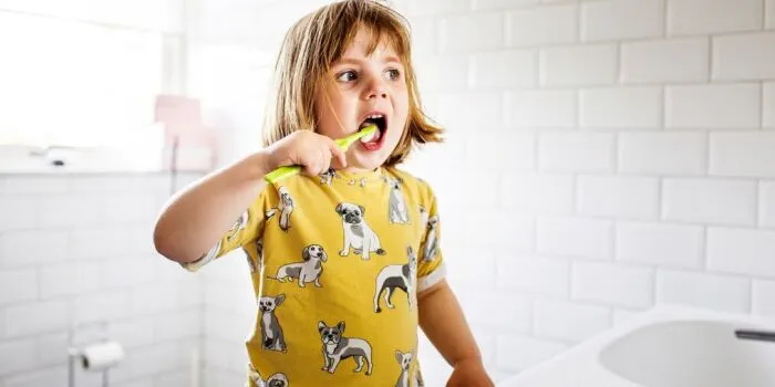 child brushing their teeth in with a yellow toothbrush
