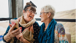 Two older adults sitting indoors, looking at a phone together