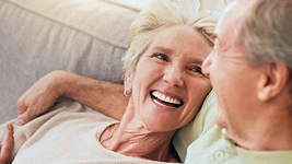 Two older adults sitting together on a sofa at home