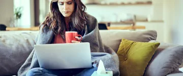 person on a sofa with a laptop, fighting a cold