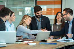 People collaborating around a table with laptops in a modern office.