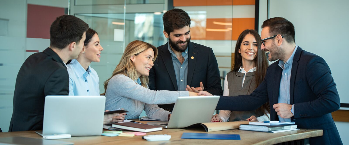 People collaborating around a table with laptops in a modern office.