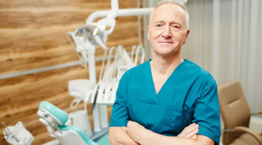 Dentist looking at camera with folded arms in dental surgery.