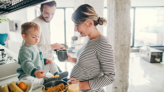Pregnant woman tasting food with toddler and husband in kitchen