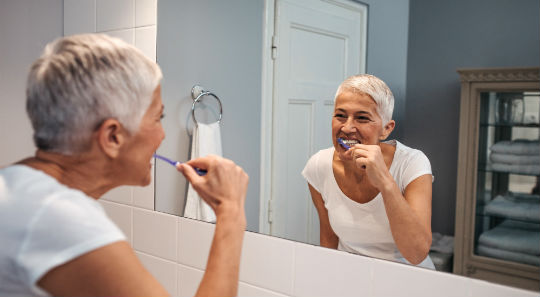 Senior woman brushing teeth in bathroom mirror