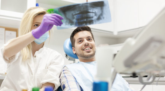 Young man in the dentist’s chair, smiling as he is treated for the effects of teeth grinding 