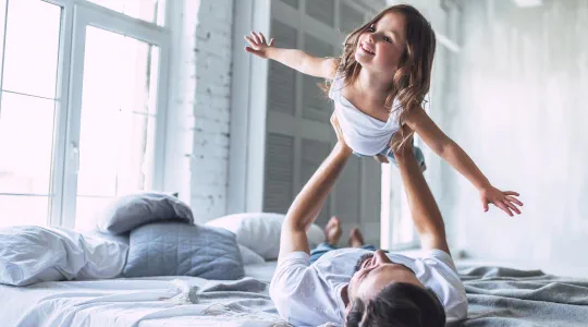Dad holding daughter in the air pretending to fly.