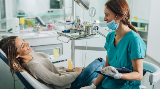Smiling woman in dentist chair with smiling clinician with face mask and clip board