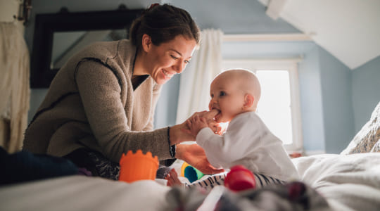 A small baby sucks on a women's finger as she smiles down at the baby