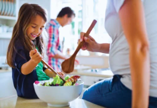 A family in the kitchen mixing a salad with wooden spoons