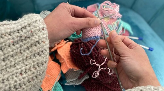 Hands using knitting needles and wool with balls of wool