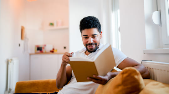 Man smiling reading book on sofa 