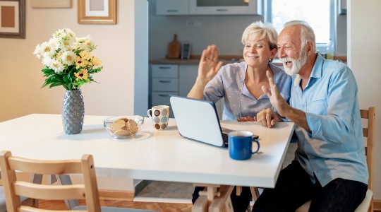 Senior couple sat at table waving on video call