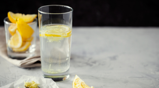 a glass of lemon water surrounded by sliced lemons on a marble work surface
