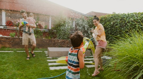 Family having water fight in garden using hosepipe and water pistols