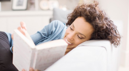 Smiling woman reading novel on sofa 