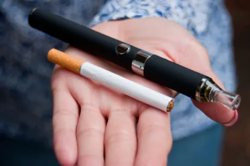 A open palm offering a cigarette and a vape pen