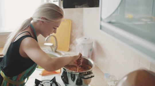 Young woman preparing soup in pot