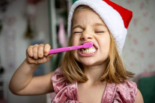 A little girl brushing her teeth in a santa hat