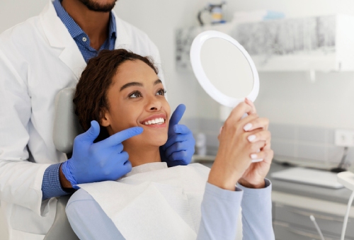 A lady admiring her smile in a mirror as her dentist points at her smile