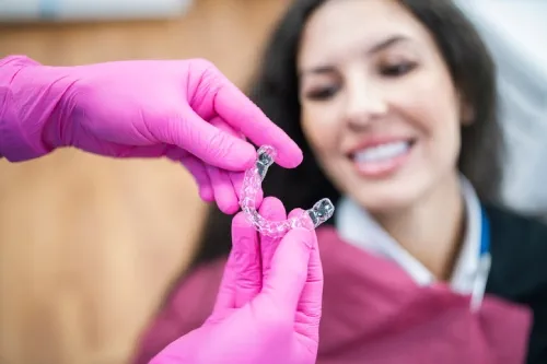 A smiling lady looking at the clear aligner her dentist is holding