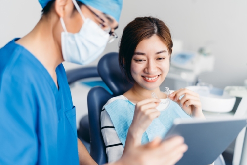 Lady holding a clear aligner while her dentist is showing her an x-ray on a tablet