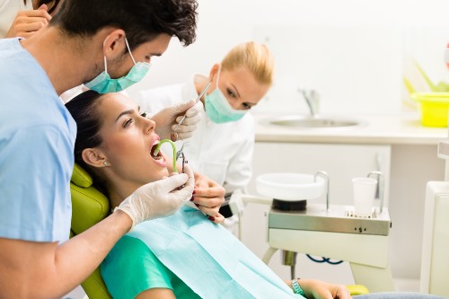 Woman in dental chair, dentist looking in her mouth