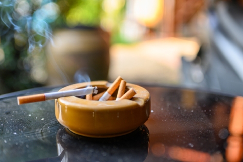 A lit cigarette in a yellow ashtray