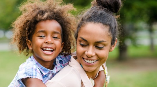 Happy mum carrying smiling toddler on back in park