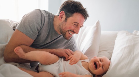 Dad tickling happy baby laying on bed