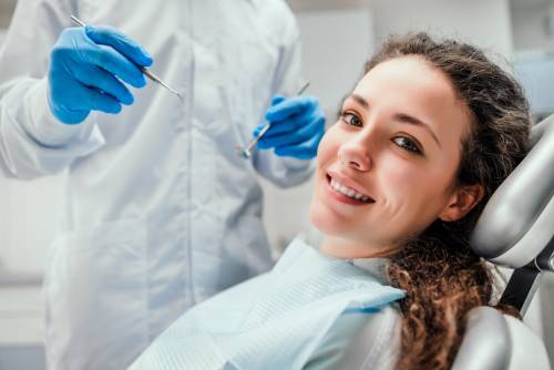 A smiling patient sits in a dental chair while a hygienist wearing surgical gloves stands alongside