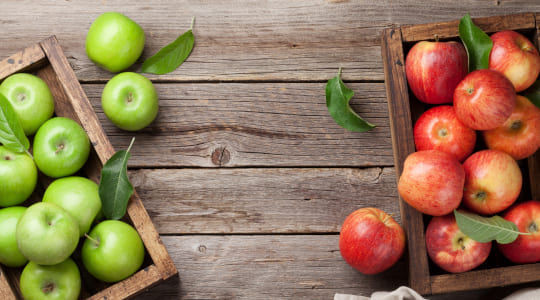 A box of green apples and a box of red apples on a wooden surface