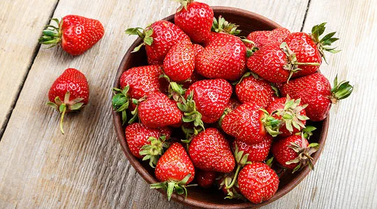 A bowl of red strawberries on a wooden surface