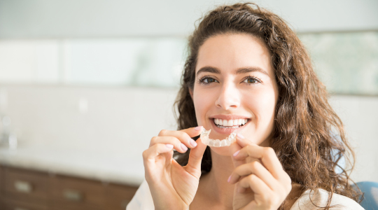 Lady smiling holding orthodontic retainer 